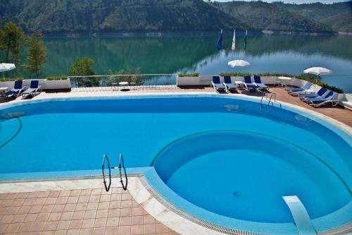 a large blue swimming pool with chairs and a lake at Lago Azul Eco Hotel in Ferreira do Zêzere