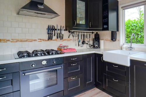 een keuken met zwarte kasten, een fornuis en een wastafel bij Better together - luxe chalet met houtkachel in Erm