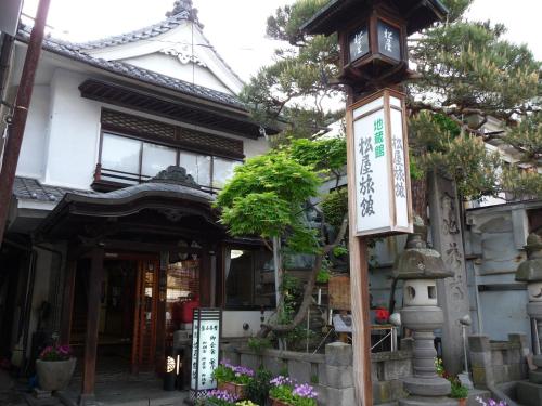 une maison avec une horloge sur un poteau en face de celle-ci dans l'établissement Jizokan Matsuya Ryokan, à Nagano