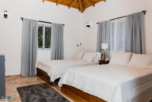 2 Betten in einem weißen Zimmer mit Fenstern in der Unterkunft Villa Anyelina Hotel Boutique in Sánchez