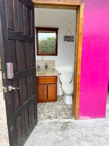 a bathroom with a toilet and a pink door at West End Cabanas in San Pedro