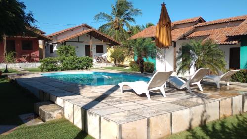 a pool with chairs and an umbrella in front of a house at Chalés do Otto e Karine in Canoa Quebrada