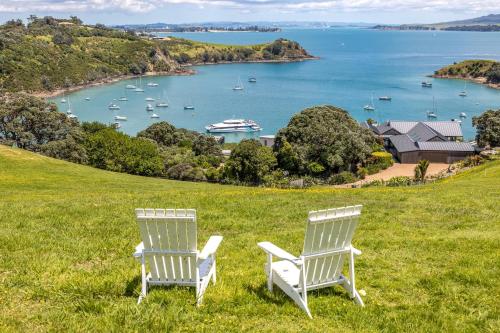two white chairs sitting on a grassy hill overlooking a harbor at The Moorings Studio Apartments in Oneroa