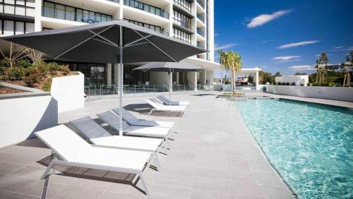 a pool with lounge chairs and an umbrella next to a building at 3BR Apartment Hinterland Views - Sierra Grand CoastHM in Gold Coast