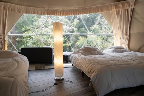 2 Betten in einem Zimmer mit einem großen Fenster in der Unterkunft glampark Shikisou Shimane in Izumo