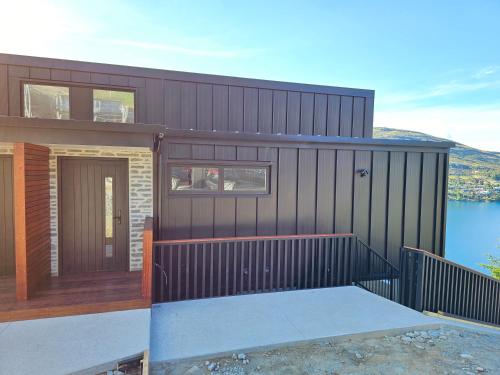 a black house with a wooden door and a body of water at Elia's House in Queenstown