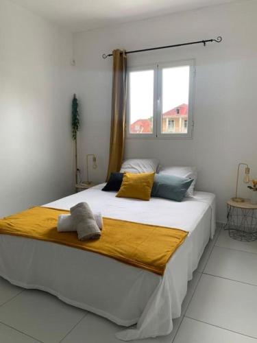 a white bedroom with a large bed with yellow and blue pillows at Studio La Caféière in Saint-Claude