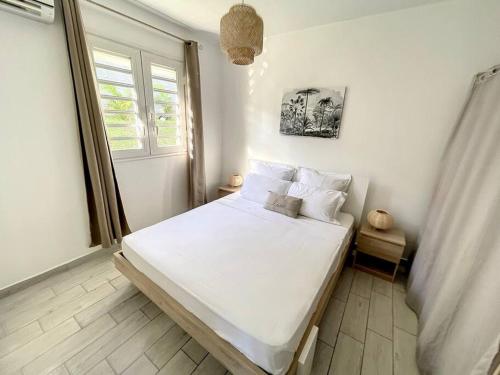 a bedroom with a bed with white sheets and a window at La Villa Rosa in Fort-de-France
