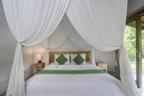 a bedroom with a white canopy bed with white curtains at Parthi Puri Ubud in Ubud