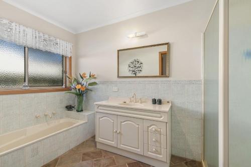 a bathroom with a sink and a bath tub and a mirror at Peaceful Retreat Surf Side Pet Friendly Outside Only in Inverloch