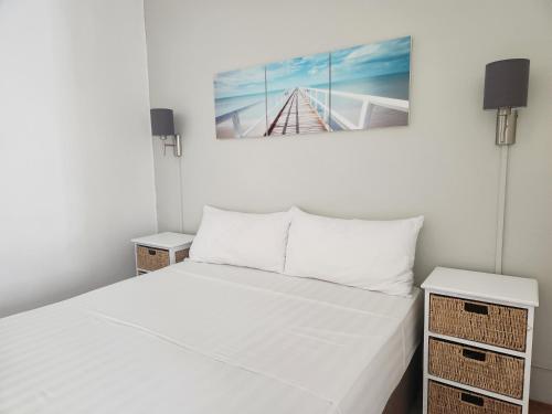 een witte slaapkamer met een bed en twee nachtkastjes bij La Perla Holiday Apartments in Pereybere