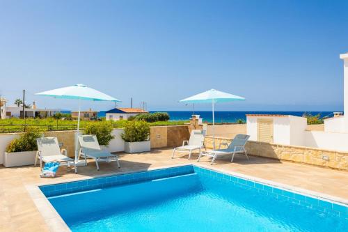a swimming pool with chairs and umbrellas on a house at Villa Diana Seaside in Pomos