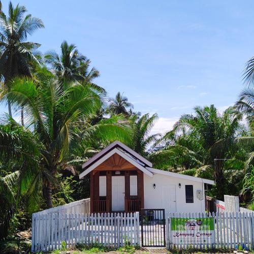 a small house behind a white fence with palm trees at Kampung Cottage Bagan Datuk in Selekoh