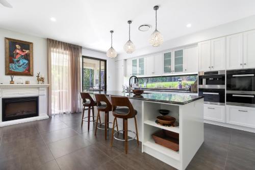 a kitchen with white cabinets and a bar with stools at Casa Bella 3 Bedroom in Coffs Harbour