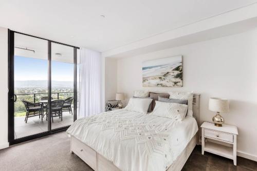 a white bedroom with a bed and a balcony at Shellharbour Lakeview Apartment in Barrack Point