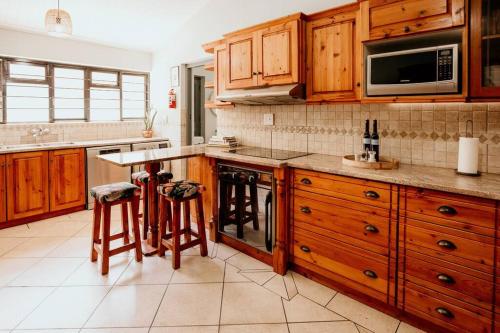 a kitchen with wooden cabinets and a counter with stools at Spacious home with pool 200M from beach in Cape Town