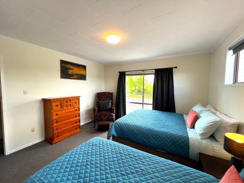 a bedroom with two beds and a chair and a window at Parkview Holiday Homes "Opposite of Famous Kuirau Park" in Rotorua