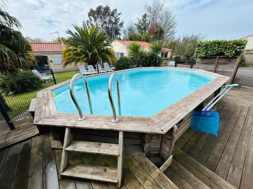 uma piscina com um deque de madeira e uma mesa de madeira em "VILLA DUPUY" Maison avec jardin clos arboré, 8 personnes, piscine bois privative em Talmont