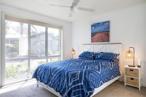 a bedroom with a bed with a blue comforter and windows at Relaxed Poolside Living in a Resort-style Setting in Safety Beach