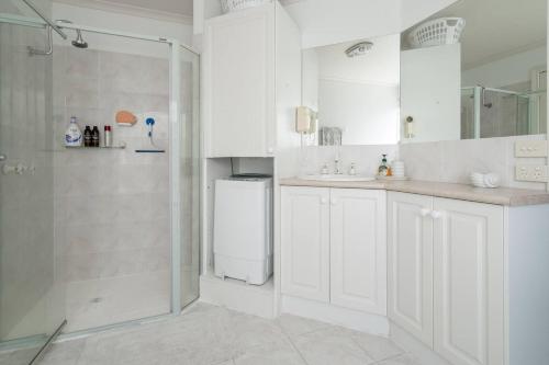 a white bathroom with a shower and a sink at Relaxed Poolside Living in a Resort-style Setting in Safety Beach