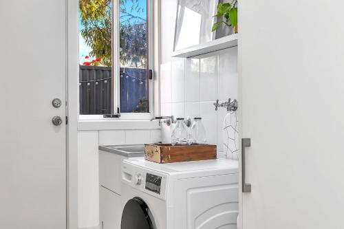 uma máquina de lavar roupa branca na casa de banho com uma janela em Shore Haven - A Relaxed Seaside Stay em Port Noarlunga