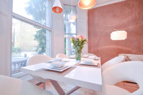 a dining room with a white table and white chairs at Stylish 2BR Designer Flat Holland Park in London