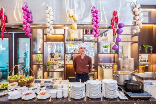 a man standing in a kitchen with plates on a table at Canvas Danang Beach Hotel in Da Nang