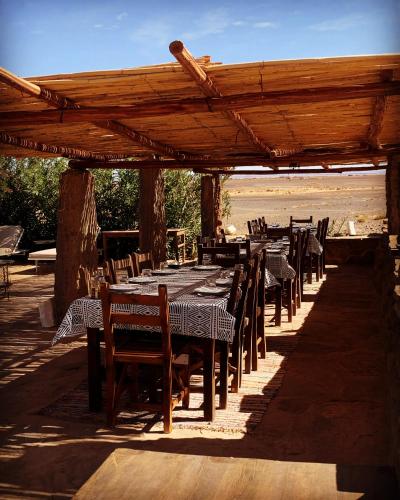 a restaurant with tables and chairs under a wooden pergola at Maison Boutchrafine in Erfoud