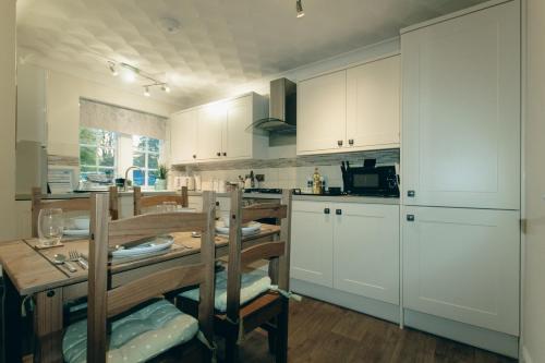uma cozinha com armários brancos e uma mesa com cadeiras em Acer Holiday Cottage Tideswell village Buxton Peak District by Rework Accommodation em Tideswell