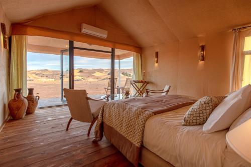 a bedroom with a bed and a large window at Erg Chebbi Luxury Desert Camp in Merzouga