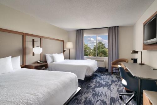 アルバニーにあるFairfield Inn & Suites by Marriott Albanyのベッド2台、デスク、窓が備わるホテルルームです。