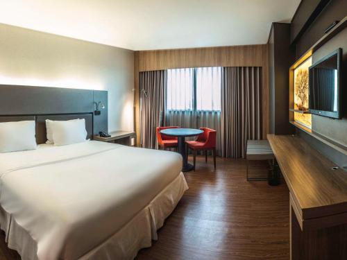 ein Hotelzimmer mit einem großen Bett und einem Schreibtisch in der Unterkunft Mercure Uberlândia Plaza Shopping in Uberlândia