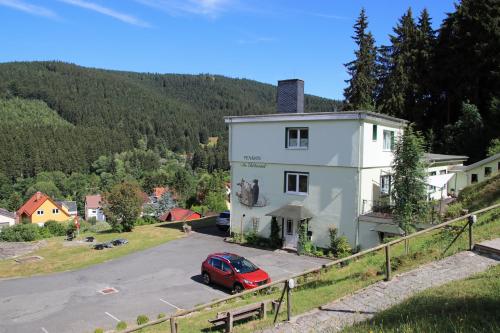 ein rotes Auto, das vor einem weißen Gebäude parkt in der Unterkunft Pension Am Waldesrand in Ilmenau