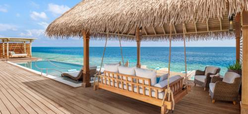 a porch with chairs and a pool and a straw umbrella at Waldorf Astoria Maldives Ithaafushi in South Male Atoll
