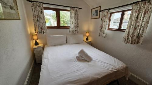 um quarto com uma cama branca e 2 janelas em Hillside Cottage em Porthscatho