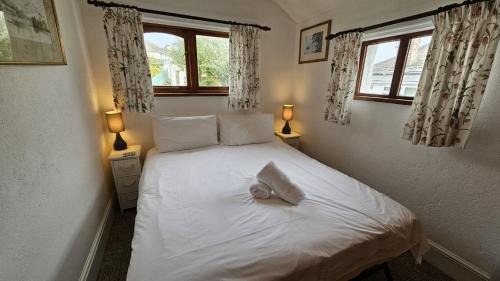 una camera da letto con un letto bianco con due finestre di Hillside Cottage a Porthscatho