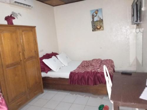 a small bedroom with a bed and a wooden cabinet at Hôtel Le Quilombo in Garoua