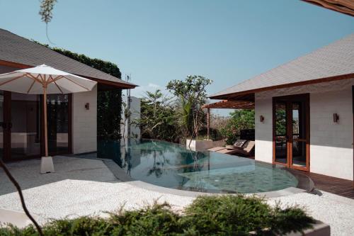 ein Pool neben einem Haus mit Sonnenschirm in der Unterkunft Poco Poco villas by Aayan in Jimbaran