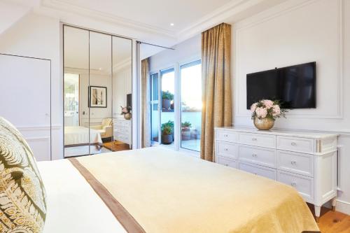 a white bedroom with a television and a dresser at Grand Hôtel Du Palais Royal in Paris