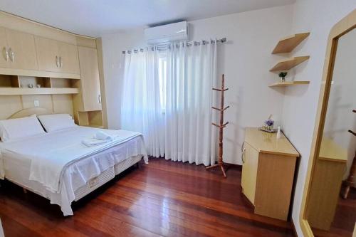 1 dormitorio con cama blanca y suelo de madera en Casa Familiar em Bento Gonçalves, en Bento Gonçalves