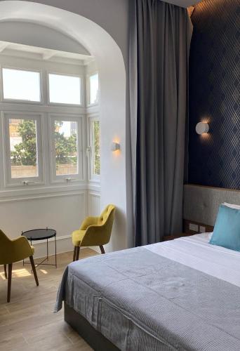 a bedroom with a bed and chairs and a window at Tritoni Valletta Boutique Hotel in Il-Furjana