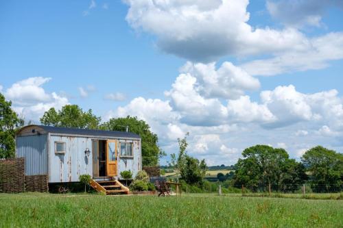 a tiny house in a field with a cloudy sky at Honey Bee - Comfortable luxury shepherds hut with hot tub in Bradpole