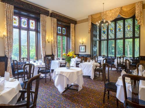 a restaurant with white tables and chairs and windows at Orton Hall Hotel & Spa in Peterborough