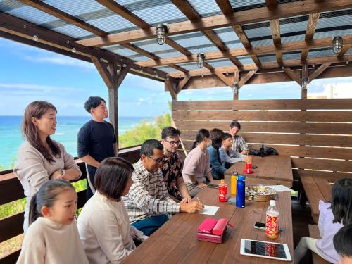 a group of people sitting at a wooden table at ペンション アラナハウス沖縄 in Toya