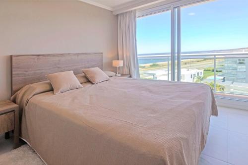1 dormitorio con 1 cama grande y ventana grande en Oceana Suites en Cruceros III, con piscina interior climatizada, en Punta del Este