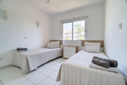 2 bedden in een witte kamer met een raam bij Iris Village Block 12-105 in Paphos City