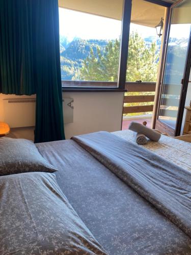 a bed in a room with a large window at Encia's Home Dolomiti in Castello di Fiemme