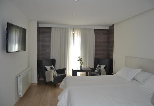 a bedroom with a large white bed and chairs at Hotel Victoria in Puebla de Sanabria
