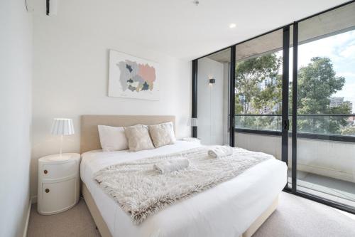 um quarto com uma grande cama branca e uma grande janela em Stunning 2br2ba Apt North Melwi-fifree Parking em Melbourne