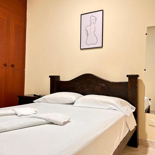 a bed with white sheets and a picture on the wall at Casa Hotel Los Fundadores in La Victoria
